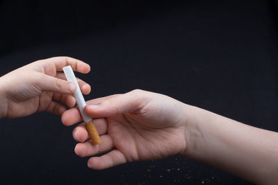 Close-up of person hand giving cigarette to child over black background