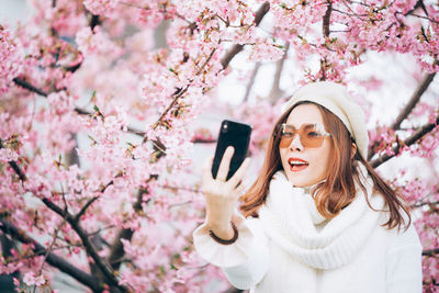 Beautiful woman taking selfie by cherry tree