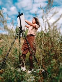 Young woman holding umbrella while standing on field