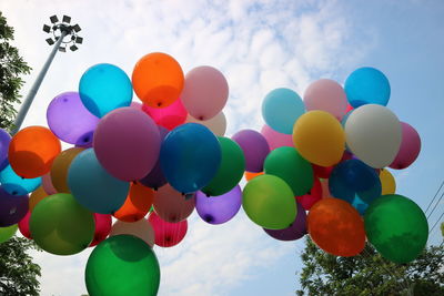 Low angle view of colorful helium balloons against sky