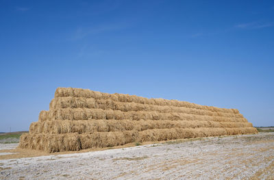 Hay bales on field against clear blue sky