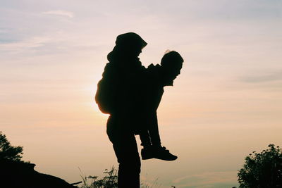 Silhouette father carrying daughter against sky during sunset