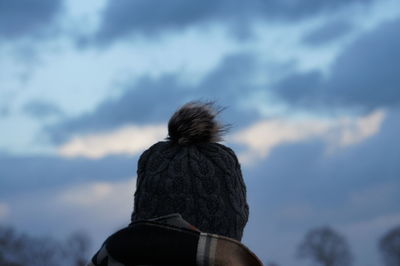 Rear view of woman wearing knit hat against cloudy sky during sunset