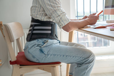 Man freelancer wearing back support belt working remotely from home