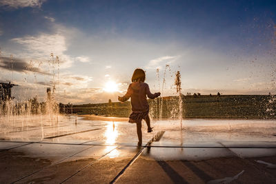 Young girl hold her foot in the water at a splash pad at sunset