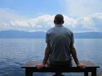 Rear view of man looking at lake against sky