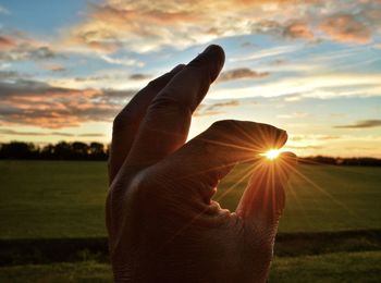 Midsection of person hand on field against sky during sunset
