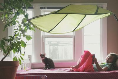 Cheerful girl lying on bed with cat against window at home