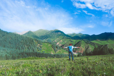 Rear view of man with arms outstretched standing on landscape against sky