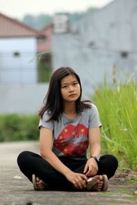 Portrait of teenage girl sitting on street by plants