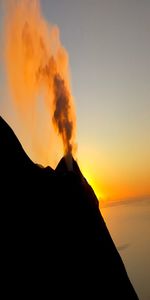 Smoke emitting from volcanic mountain against sky during sunset