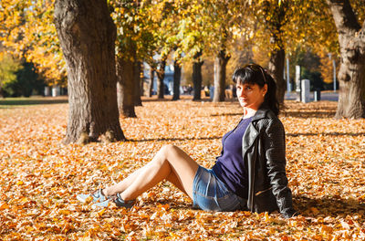Side view full length portrait of woman sitting at park during autumn on sunny day