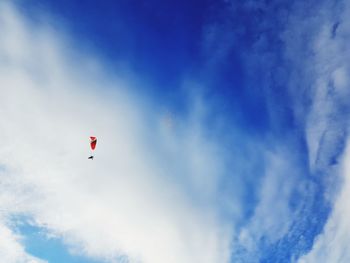 Low angle view of people paragliding against blue sky