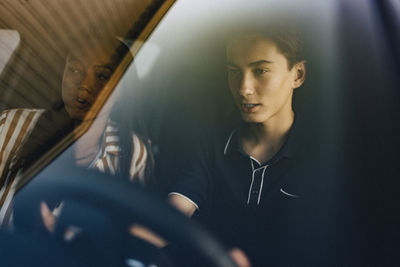 Focused teenage boy learning driving lessons from mother while sitting in car seen through windshield