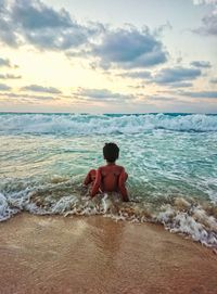 Rear view of shirtless boy in sea against sky