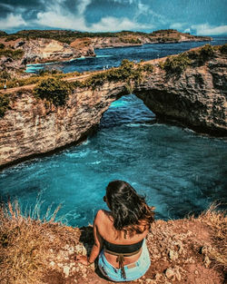 Rear view of woman sitting on rock by sea