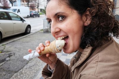 Close-up portrait of woman eating ice cream cone on sidewalk