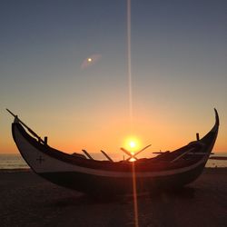 Boat moored on beach against sky during sunset