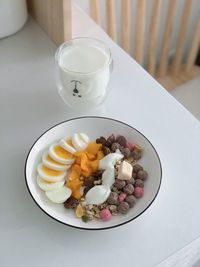 There are sliced eggs, fresh fruit and some cereal on the white plate