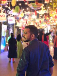 Rear view of smiling young man looking away against illuminated decoration in city at night