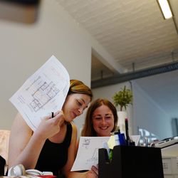 Happy female colleagues discussing blueprints in office