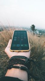 Midsection of person holding camera on field against sky