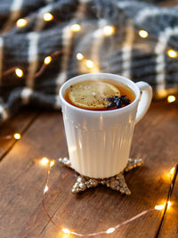 White cup of hot tea with lemon. cozy decorations - grey knitted sweater and light bulbs on wood.
