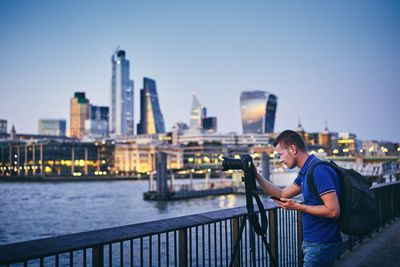 Man photographing while standing by railing in city at dusk