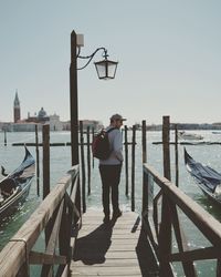 Rear view of man standing on pier at sea against sky
