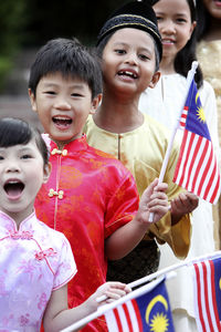 Portrait of cute friends in traditional clothing holding malaysia flags