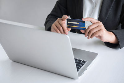 Midsection of businesswoman holding credit card by laptop on table