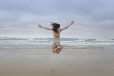 Woman jumping on beach against sky