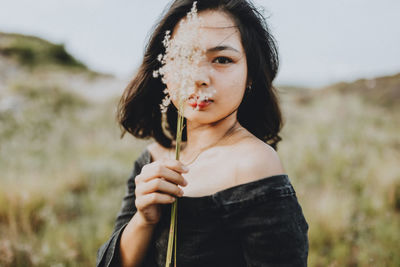 Portrait of young woman holding sunglasses on field