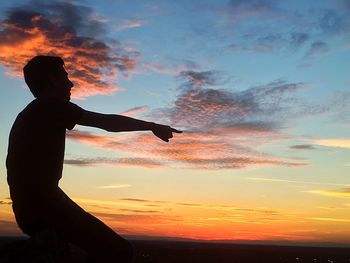 Silhouette young man pointing against sky during sunset