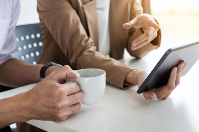 Midsection of woman holding coffee while sitting on table