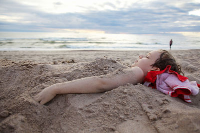 Girl lying on sand at beach against sky
