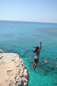 Rear view of woman on rock in sea against clear sky