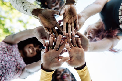 From below of group of multiracial cheerful women standing together and stacking hands in name of unity and friendship