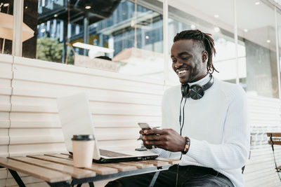 Man holding smart phone while sitting on laptop