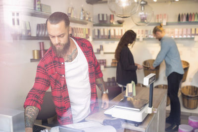 Owner standing at checkout counter while customers shopping in background