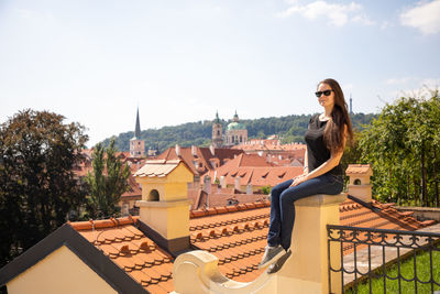 Portrait of woman sitting on wall against townscape