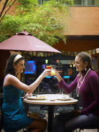 Cheerful female friends toasting drinks while sitting at outdoor cafe