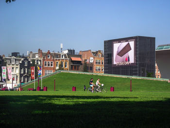 People playing on field by buildings against clear sky