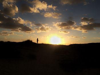 Silhouette of man on landscape against sunset sky