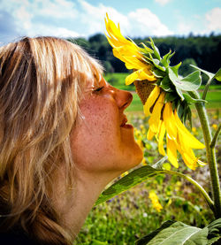 Close-up of woman smelling sunflower against sky