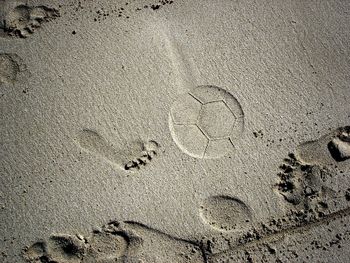 Close-up of foot and soccer ball imprints on beach sand