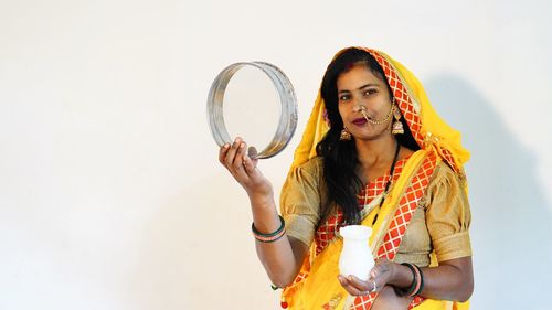 Portrait of young woman standing against white background. happy karva chauth festival