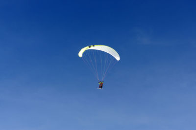 Low angle view of person paragliding against blue sky