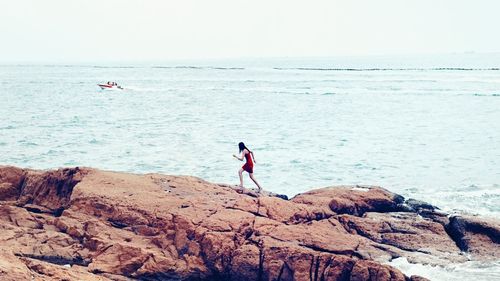 People on rock by sea against sky