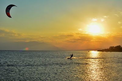 Silhouette person surfing in sea against sky during sunset